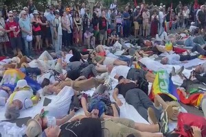 Die-in al Colosseo durante il corteo di Stop Rearm Europe.  In primissimo piano, con camicetta scura e pantaloncini beige, si vede Luke Alden, uno degli intervistati di questo articolo.